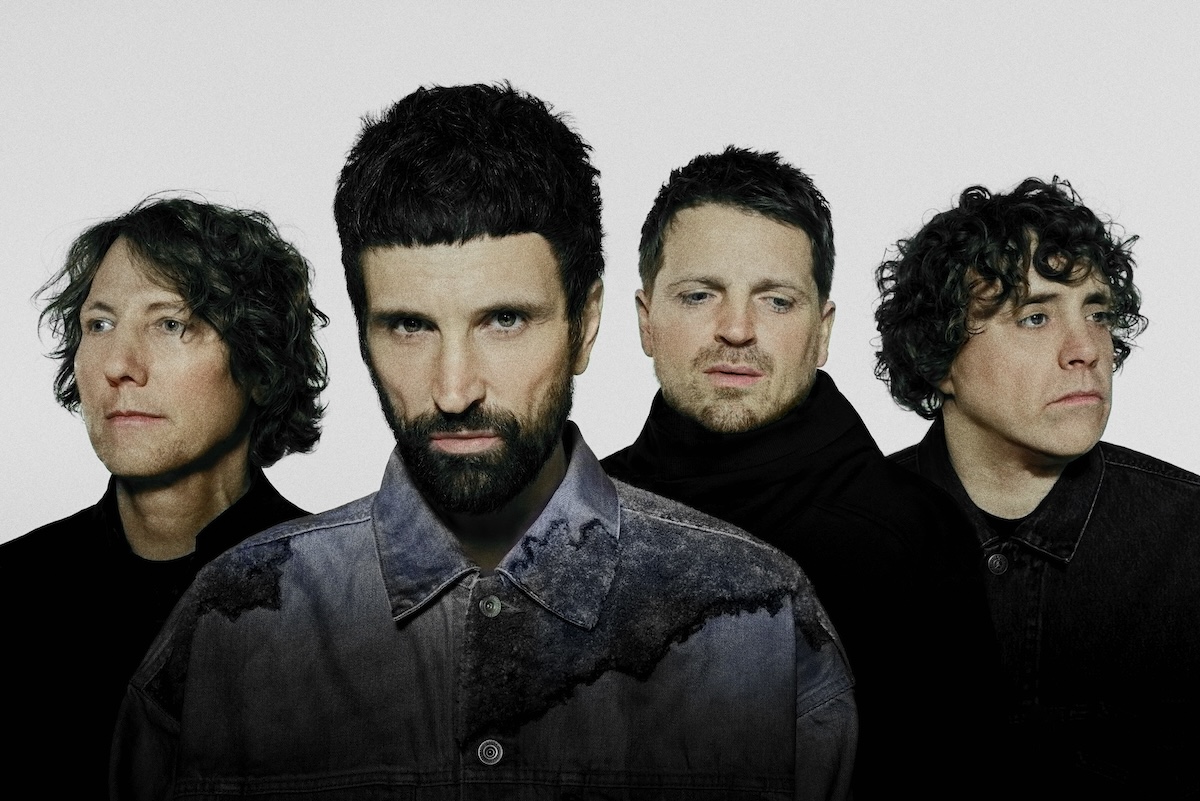 English rock band Kasabian members posing in a close-up group portrait against a plain light grey background.
